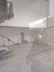reflection of man in window - inside there is concrete with old glue from carpet and a dusty metal spiral staircase